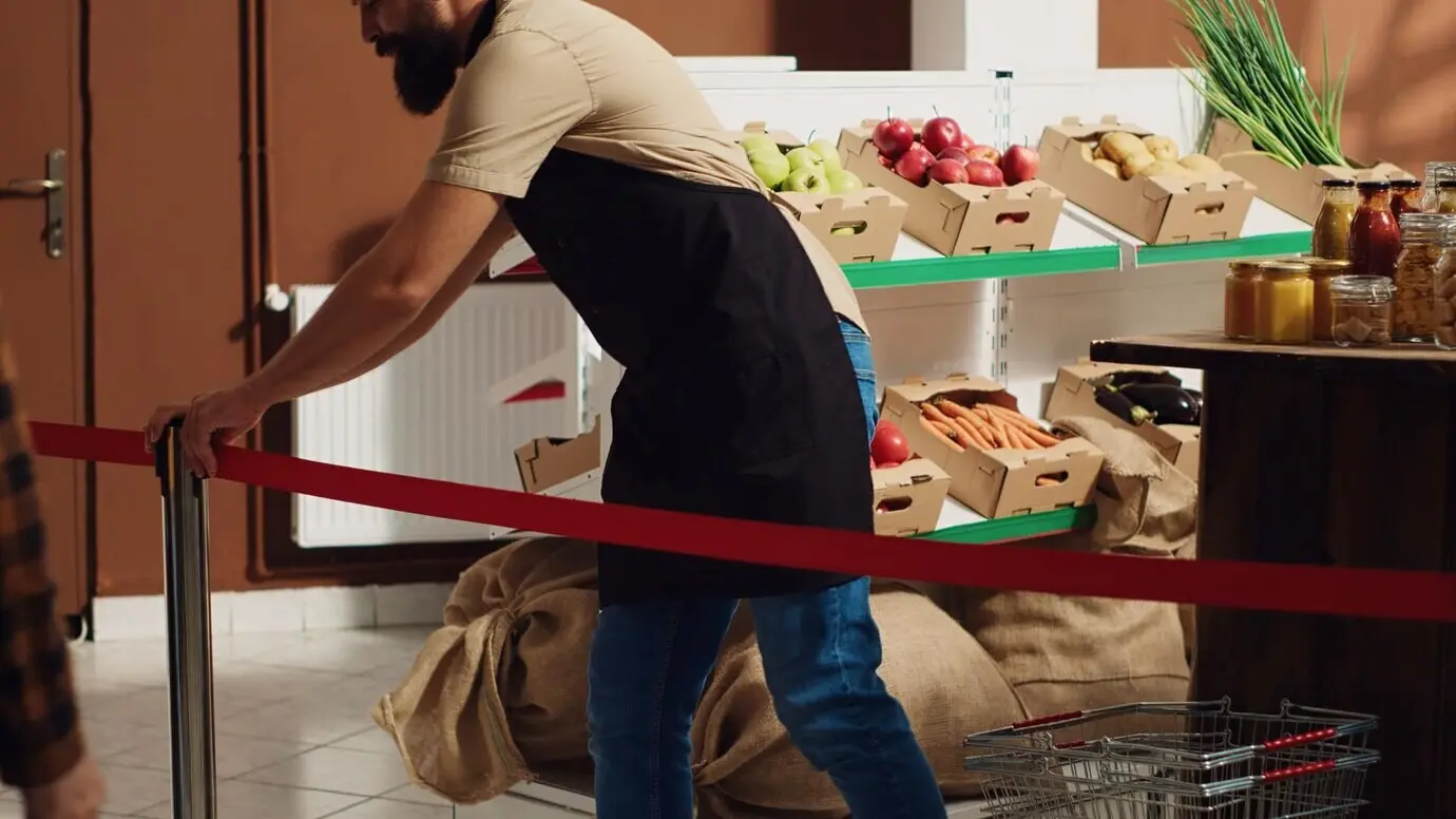 Ein Verkäufer begrüßt die ersten Kundinnen und Kunden bei der großen Eröffnungsfeier eines Zero-Waste-Supermarkts und entfernt das rote Band. Ein Ladenmitarbeiter heißt die Einkaufenden im umweltfreundlichen lokalen Nachbarschaftsladen willkommen.